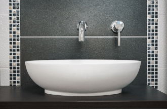 This is a photo of a sit on basin won a black unit with black tiles, mosaic tiles and white tiles and a wall-mounted single-lever basin tap